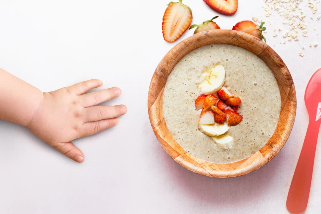 Baby reaching for porridge with fruit slices.