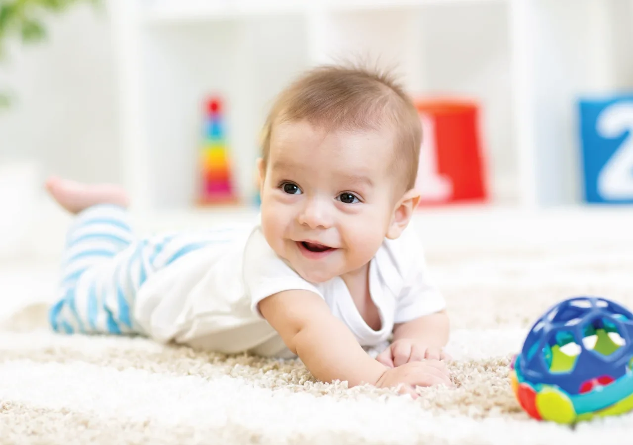 Smiling baby lying on the floor with toy.
